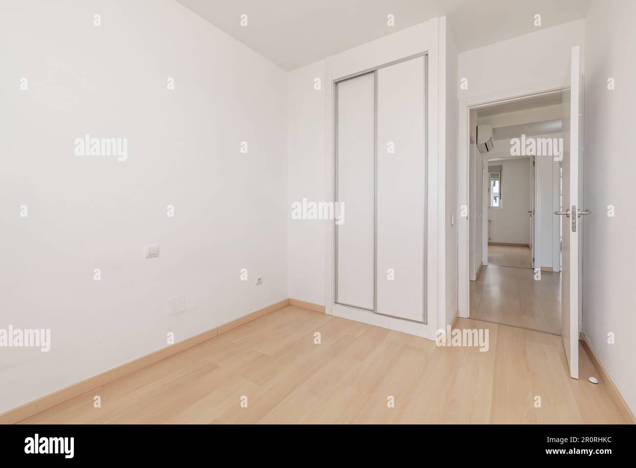 An empty room in an apartment with a built-in wardrobe with white sliding doors, light wooden flooring and white access doors Stock Photo