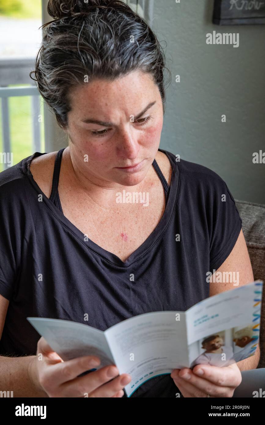 Close-up vertical image of young 30s female reading skin cancer literature on couch at home upon recent skin cancer diagnosis. Stock Photo