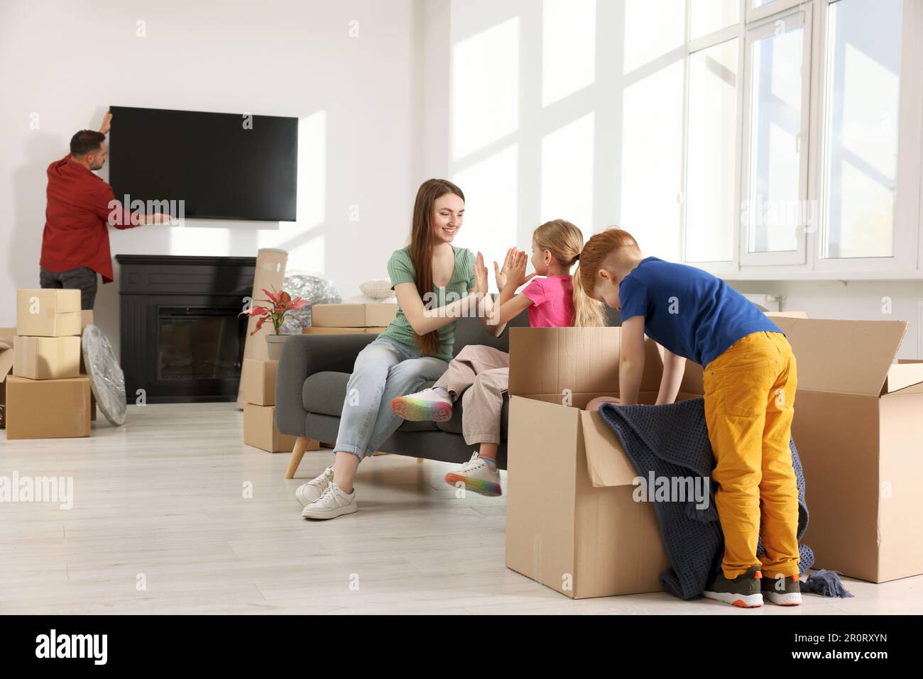 Family settling into new home. Dad setting up TV, happy mom and ...