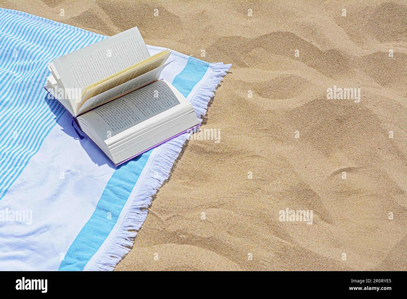 Beach towel with open book on sand, space for text Stock Photo - Alamy