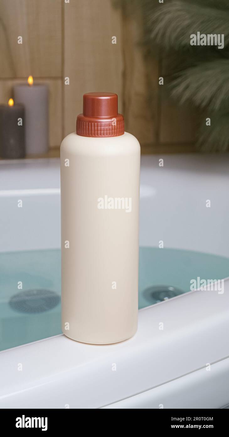 Beige bottle of bubble bath and candles on tub indoors Stock Photo