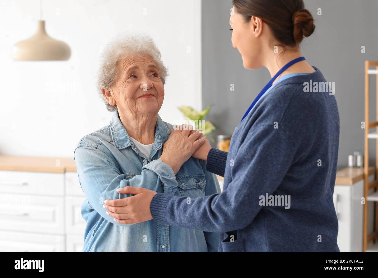 Young caregiver with senior woman hugging in kitchen Stock Photo - Alamy