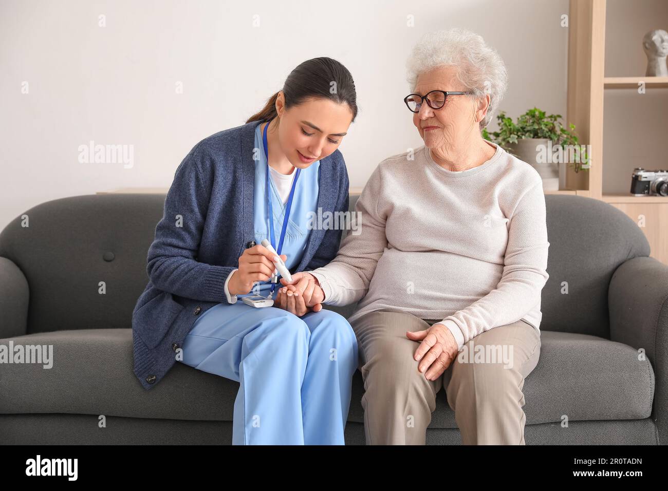 Young caregiver measuring sugar level of senior woman at home Stock Photo