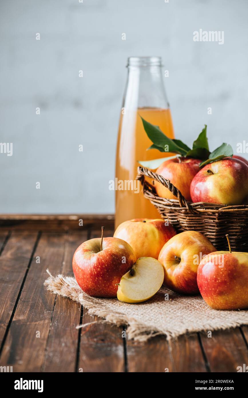 Glass bottle of apple juice and apples in basket on wooden tabletop Stock Photo
