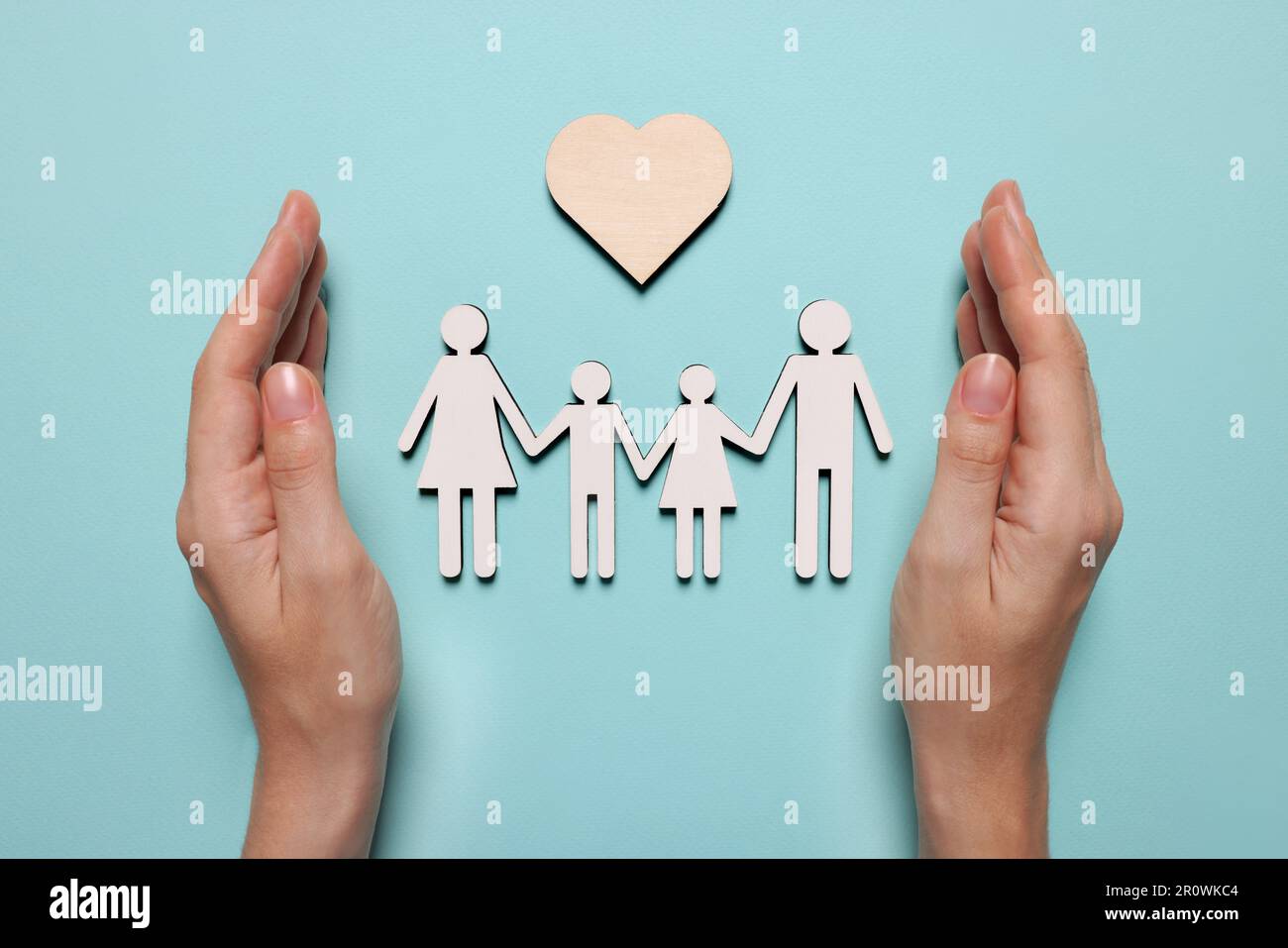Woman protecting figures of family and heart on light blue background, top view. Insurance concept Stock Photo