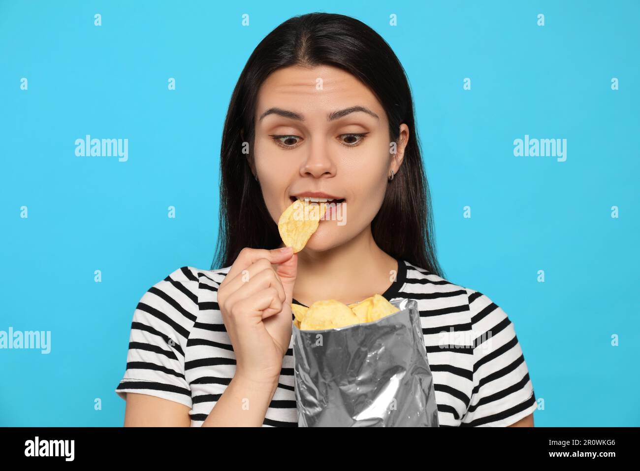 Beautiful woman eating potato chips on light blue background Stock