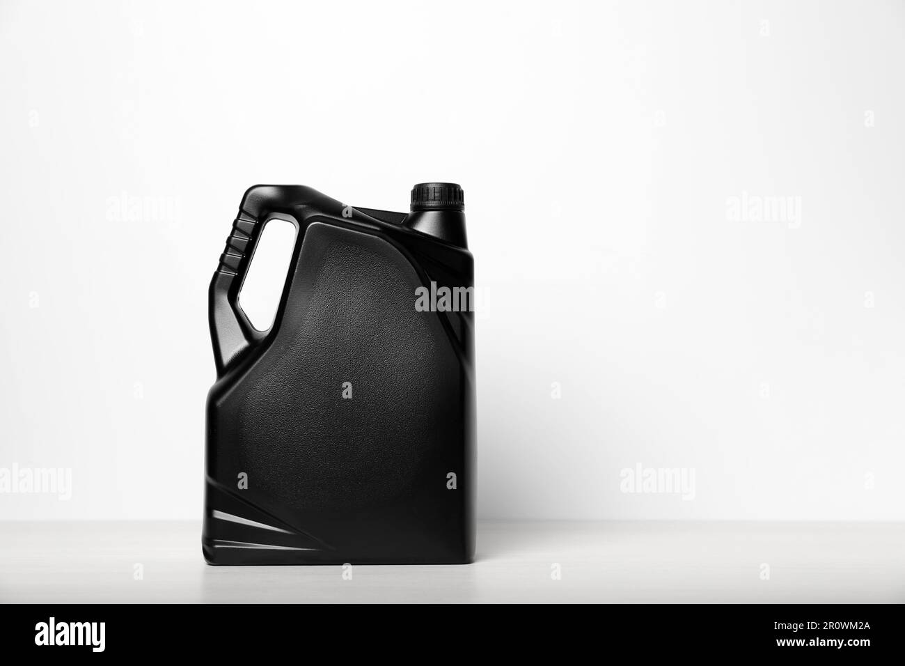 Motor oil in black canister on table against white background, space