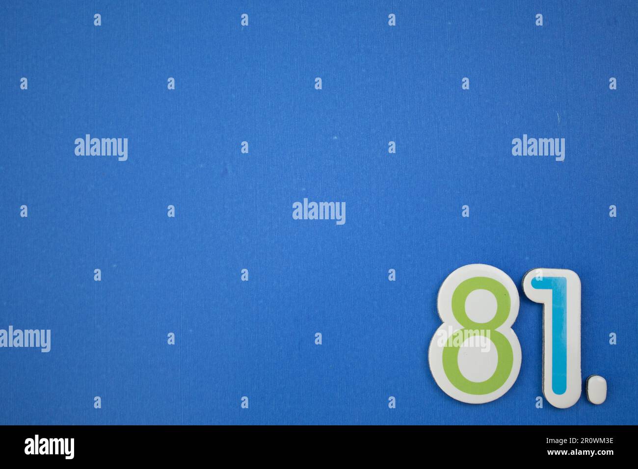 The number 81, placed on the edge of a blue background, photographed from above, colored green and light blue. Stock Photo