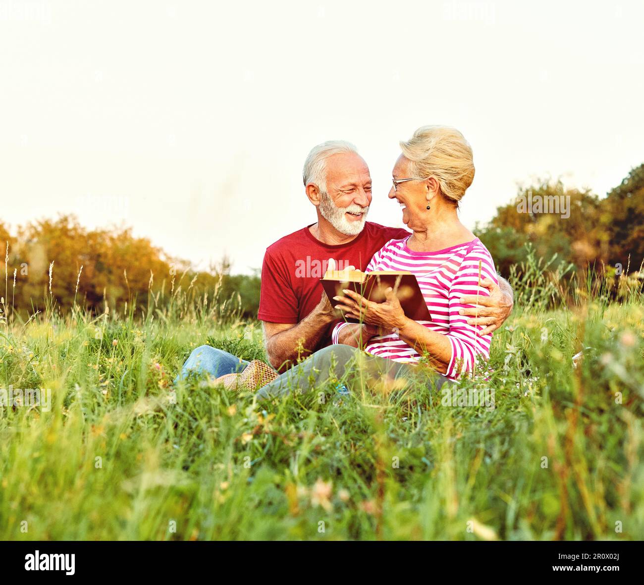 woman man outdoor senior couple happy lifestyle retirement together smiling love reading nature book Stock Photo