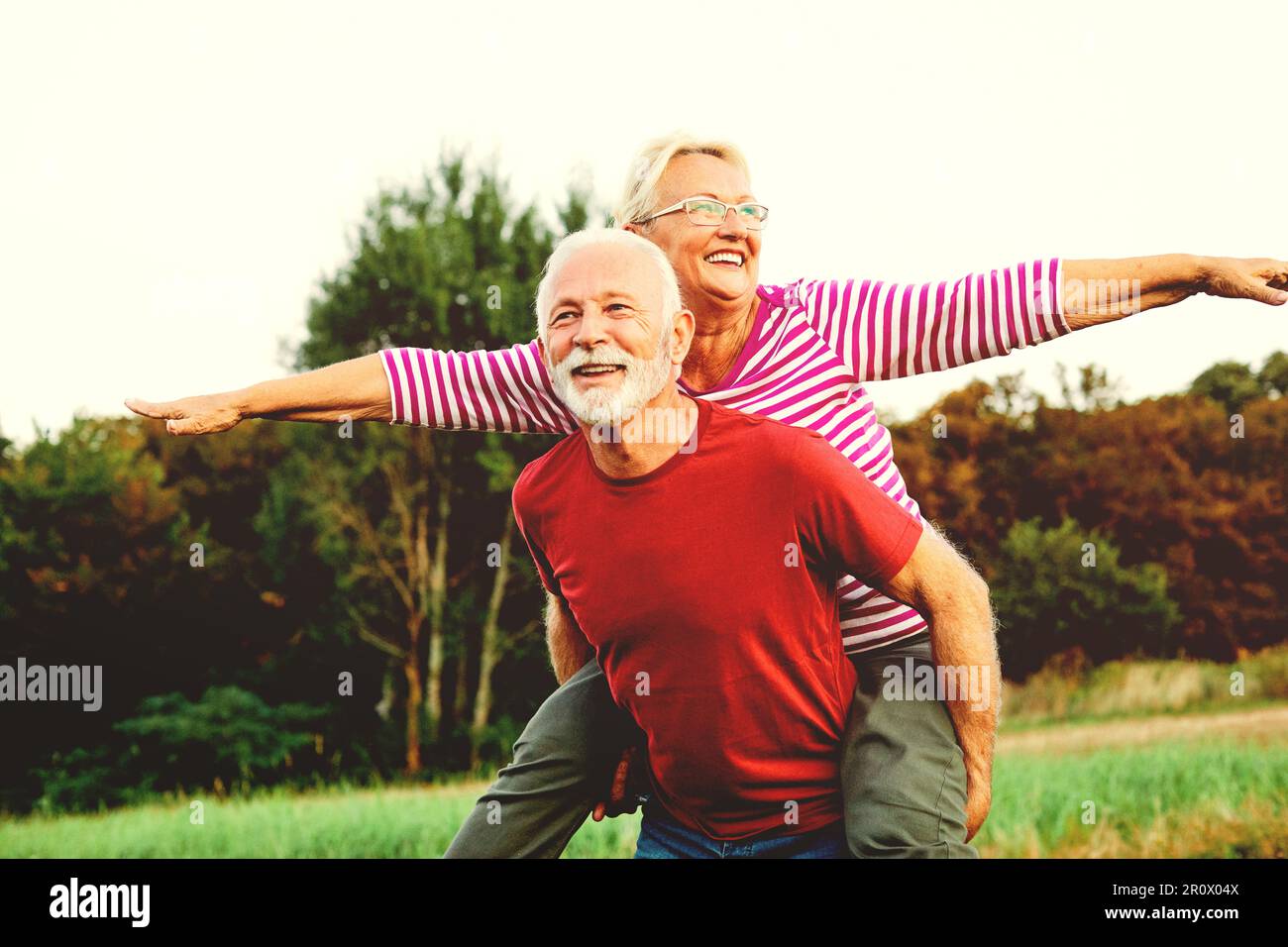 woman man outdoor senior couple happy lifestyle retirement together smiling love piggyback active mature Stock Photo