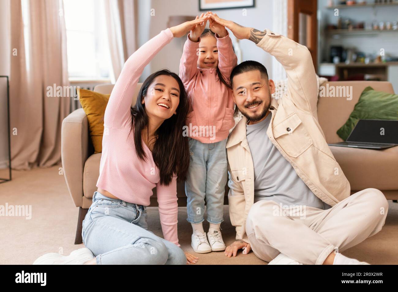 Asian Family With Child Celebrating Homeownership Doing Roof Gesture Indoors Stock Photo