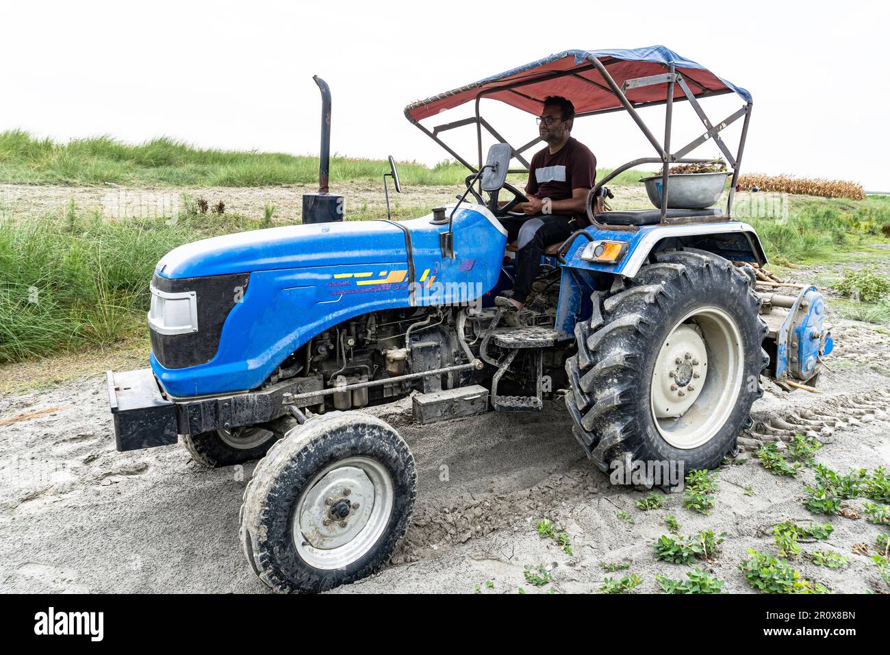 A young man driving a tractor in the field, a male driver operating a ...