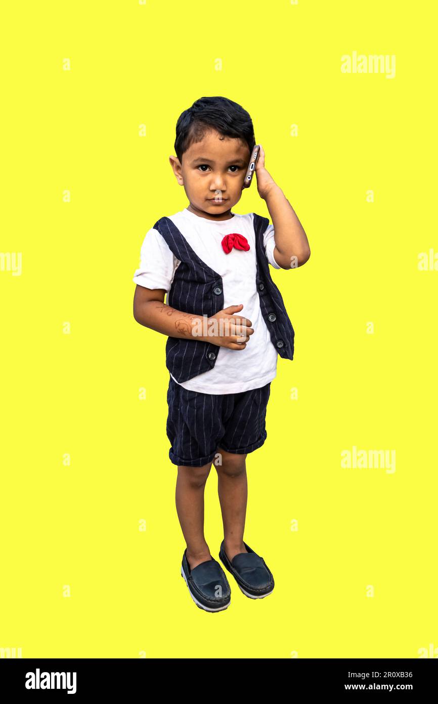 a cute boy talking on a cell phone. A little kid having a serious smartphone talking to him was isolated on the yellow background. Stock Photo