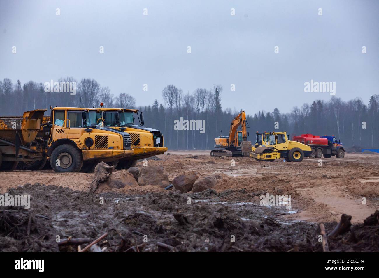 Ust-Luga, Leningrad oblast, Russia - November 16, 2021: Asphalt compactor, excavator and Komatsu dump trucks on dirty ground road Stock Photo