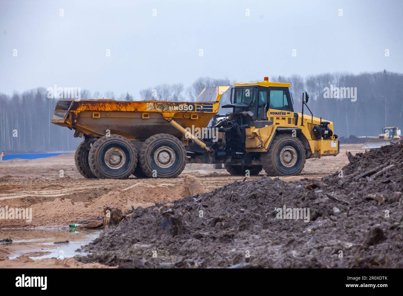 Ust-Luga, Leningrad oblast, Russia - November 16, 2021: Komatsu heavy dump truck moving ground on construction site. Forest in background. Stock Photo