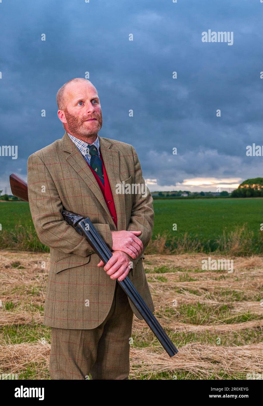An English gentleman stood at twilight in a tweed shooting suit with a shotgun Stock Photo