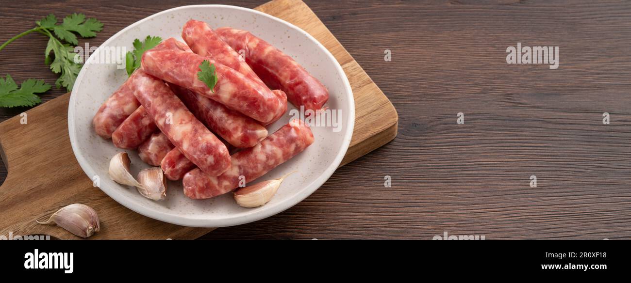 Raw Taiwanese sausage in garlic flavor with garlic cloves in a plate on wooden table background. Stock Photo