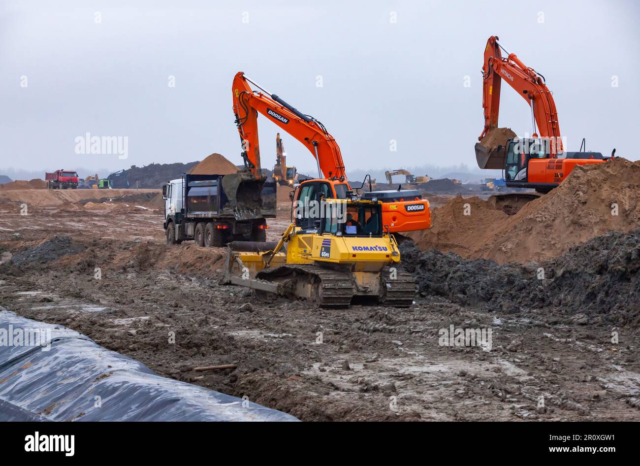 Ust-Luga, Leningrad oblast, Russia - November 16, 2021: Excavators Doosan and Hitachi, dozer Komatsu and dump truck on construction site. Rainy day, d Stock Photo