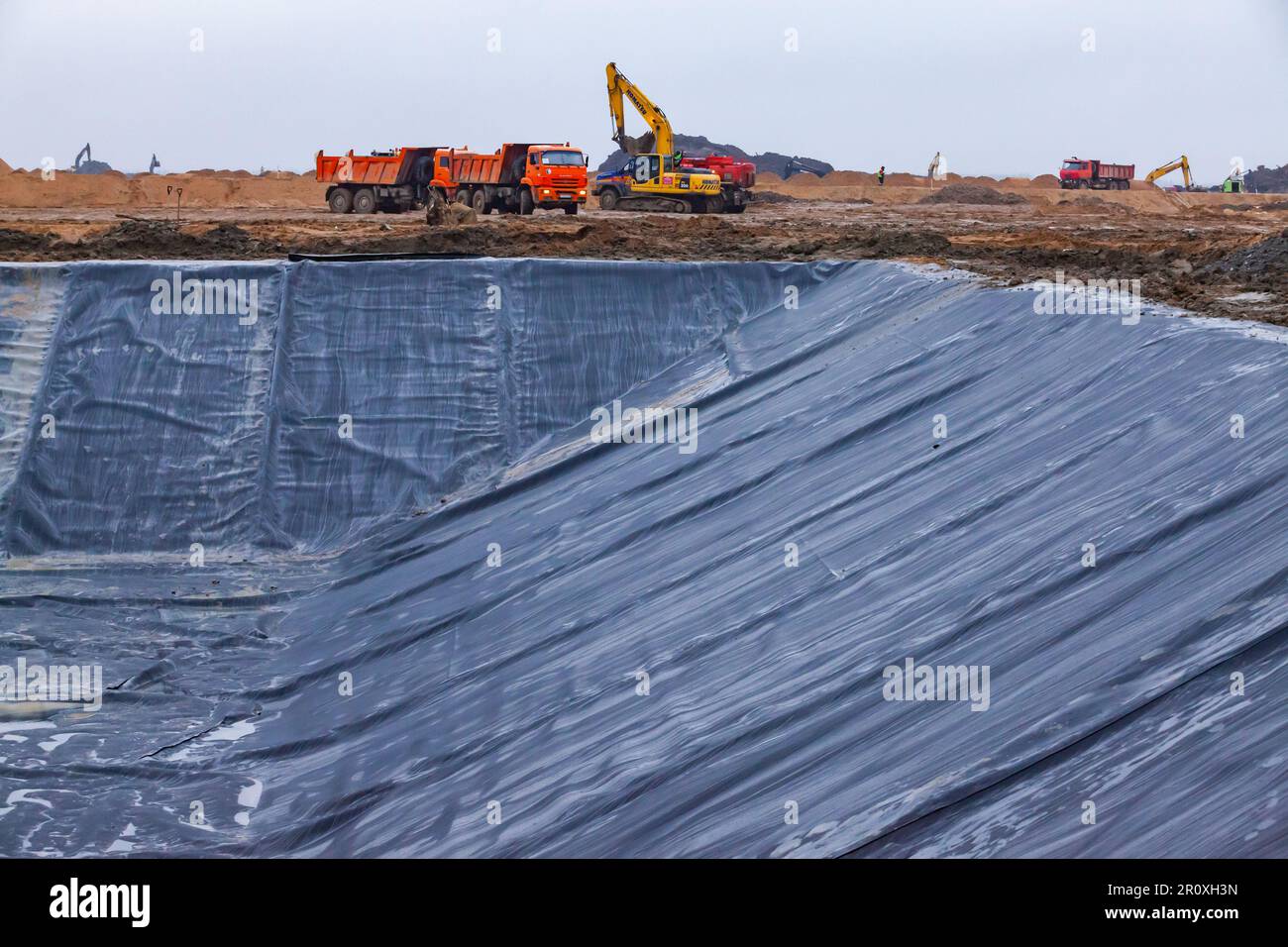 Ust-Luga, Leningrad oblast, Russia - November 16, 2021: Construction of chemical waste ditch (on front). Plastic cover of pit. Excavator and dump truc Stock Photo