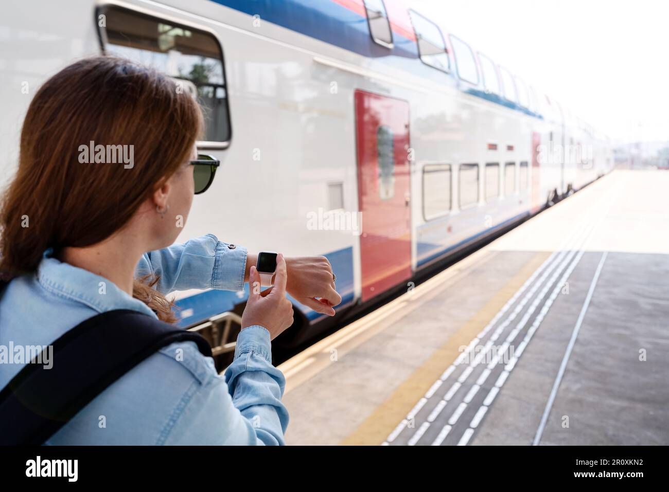 Woman waiting to board the train and looking at her wrist watch. Stock Photo