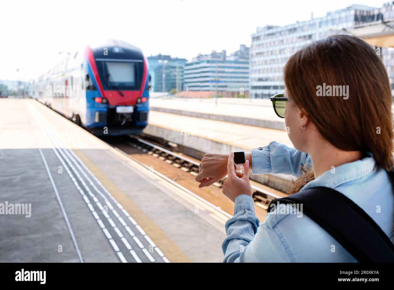 The passenger missed the train. A woman stands on the station platform and checks the time on her wrist watch. Stock Photo