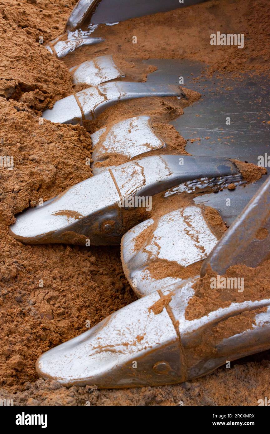 Excavator bucket steel teeth close up on Yellow sand background. Stock Photo