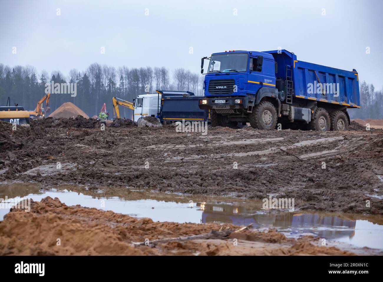 Ust-Luga, Leningrad oblast, Russia - November 16, 2021: Dump trucks moving ground on groundworks. Forest on background Stock Photo