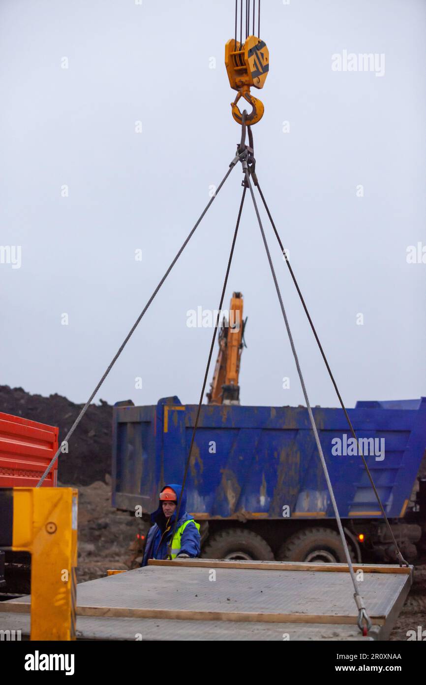 Ust-Luga, Leningrad oblast, Russia - November 16, 2021: Lifting concrete plate with mobile crane. Worker operator is out of focus Stock Photo