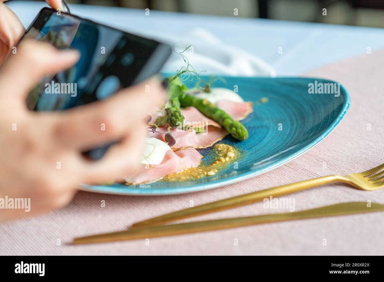 Appetizer with rosemary ham,asparagus,peanuts,and taleggio on the blue plate. A woman taking a photo of the food with a mobile phone. Stock Photo
