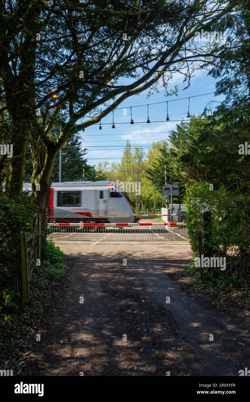 Rural railway level crossing framed by trees. Church Lane crossing in Margaretting, Essex, UK with Greater Anglia train passing. Crossing gates closed Stock Photo