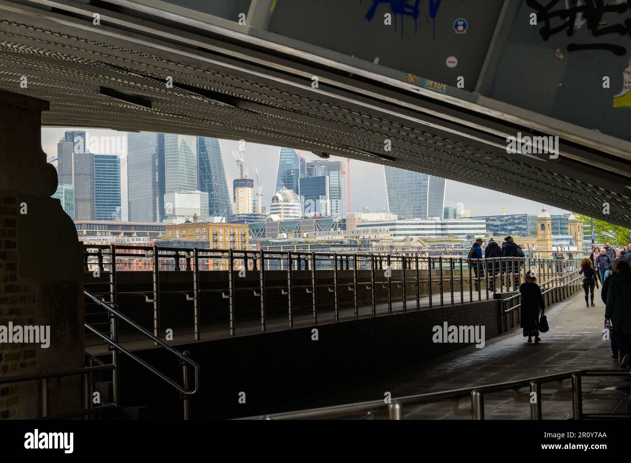 LONDON - April 21, 2023: A striking view of the City of London from beneath Blackfriars Bridge, with pedestrians walking in silhouette. Stock Photo