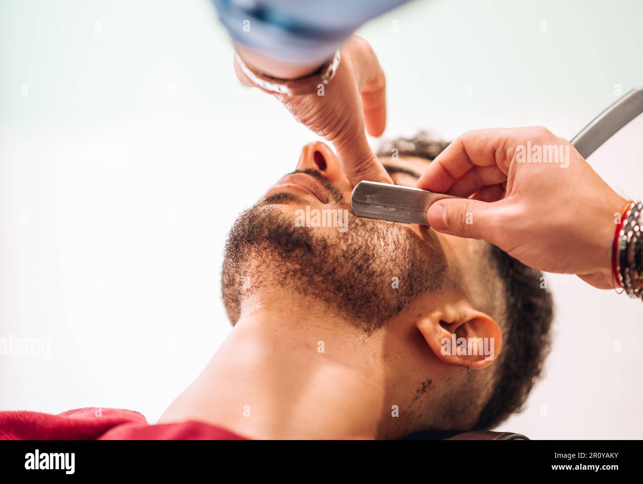 Unrecognizable barber cutting beard of calm male client with sharp razor in barbershop Stock Photo