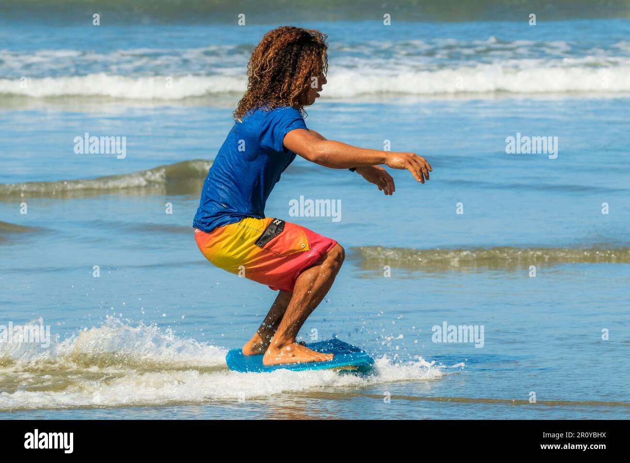 Young man with long hair using a boogie board as a skimboard at this hip surf beach & yoga destination. Playa Guiones, Nosara, Guanacaste, Costa Rica Stock Photo