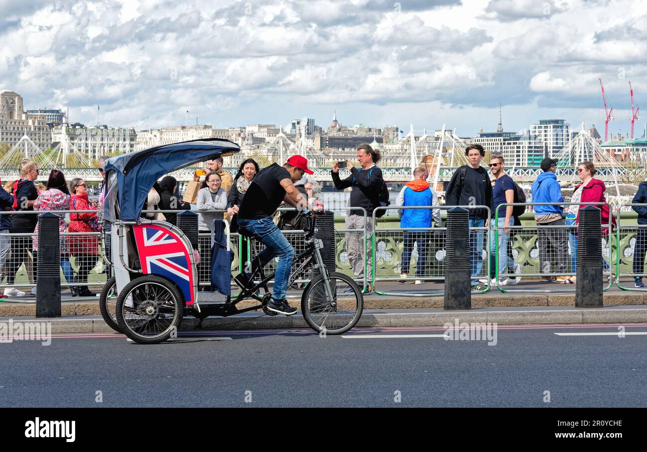 A London Rickshaw or Pedicab operating on Westminster Bridge crowded with tourists on a sunny spring day Central London England Great Britain UK Stock Photo