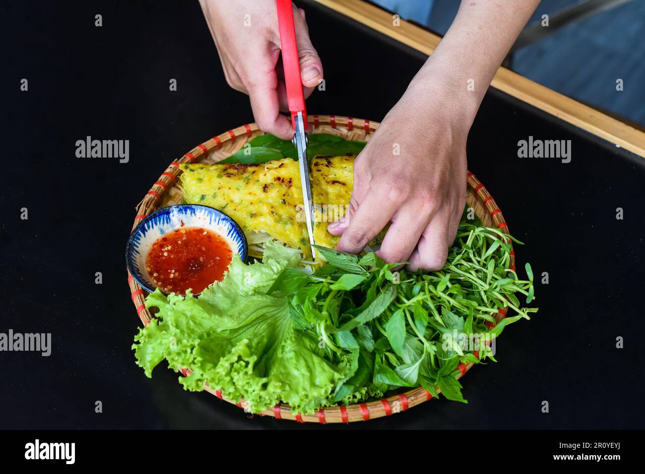 Hands with scissors cutting Vietnamese pancake Banh xeo with sea food on black background top view Stock Photo