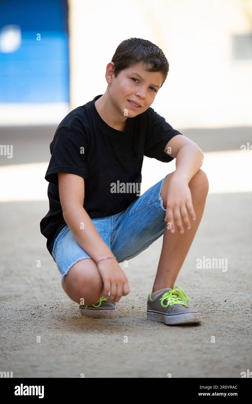 Boy in shorts and black t-shirt crouching while looking at the camera ...