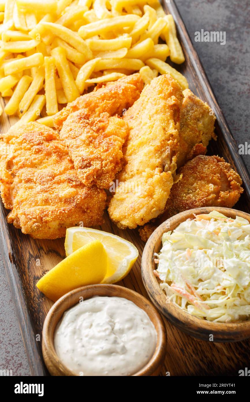 Fish Fry is accompanied by coleslaw, French fries, tartar sauce closeup on the wooden board on the table. Vertical Stock Photo