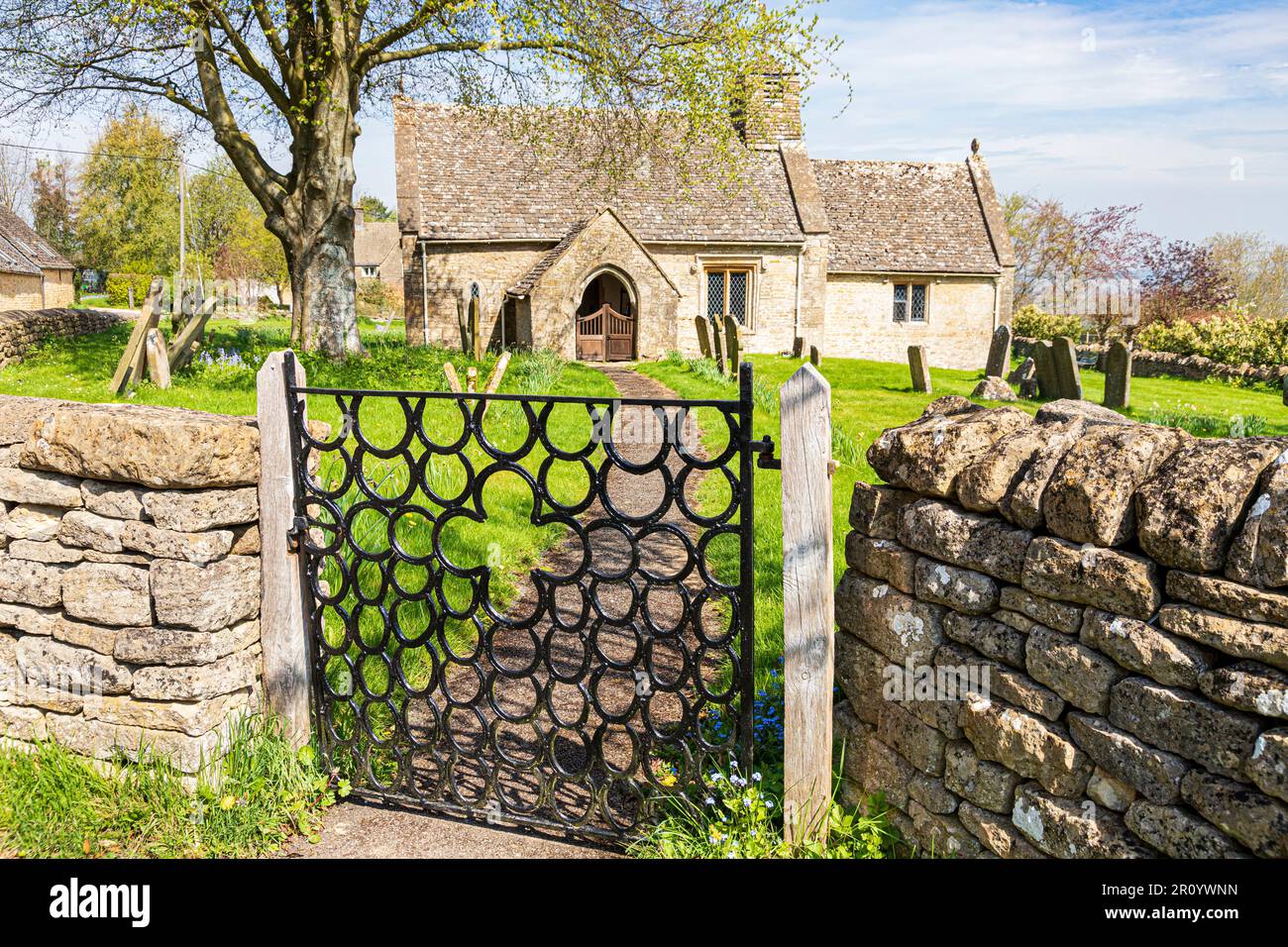 Church of St. James in the Cotswold village of Clapton-on-on-the-Hill, Gloucestershire UK. Wrought iron horseshoe gate was made by Raymond Phillips. Stock Photo