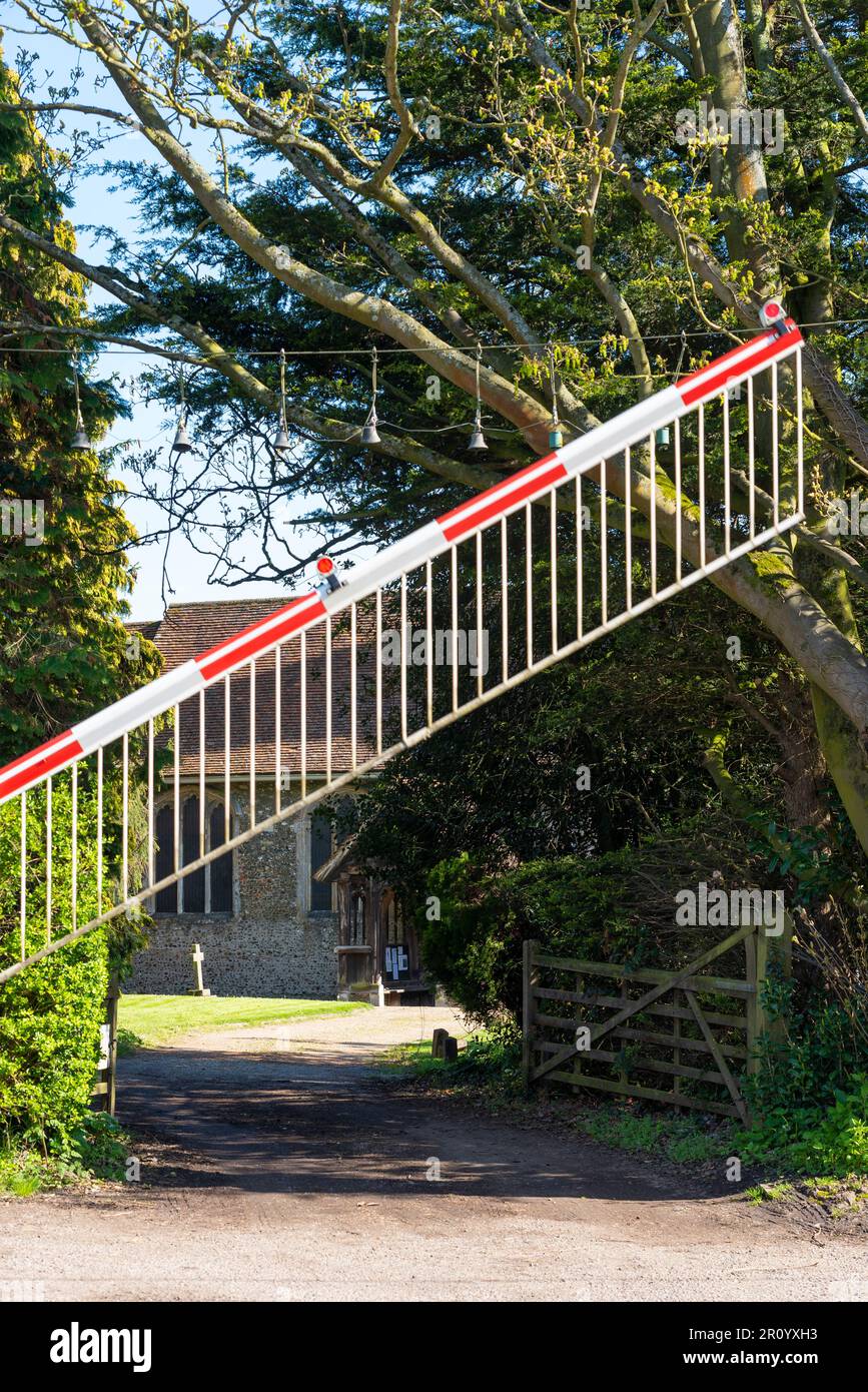 Railway level crossing with gates coming down in rural area. Church Lane, Margaretting, Essex, leading to church. Old bell warning system over road Stock Photo