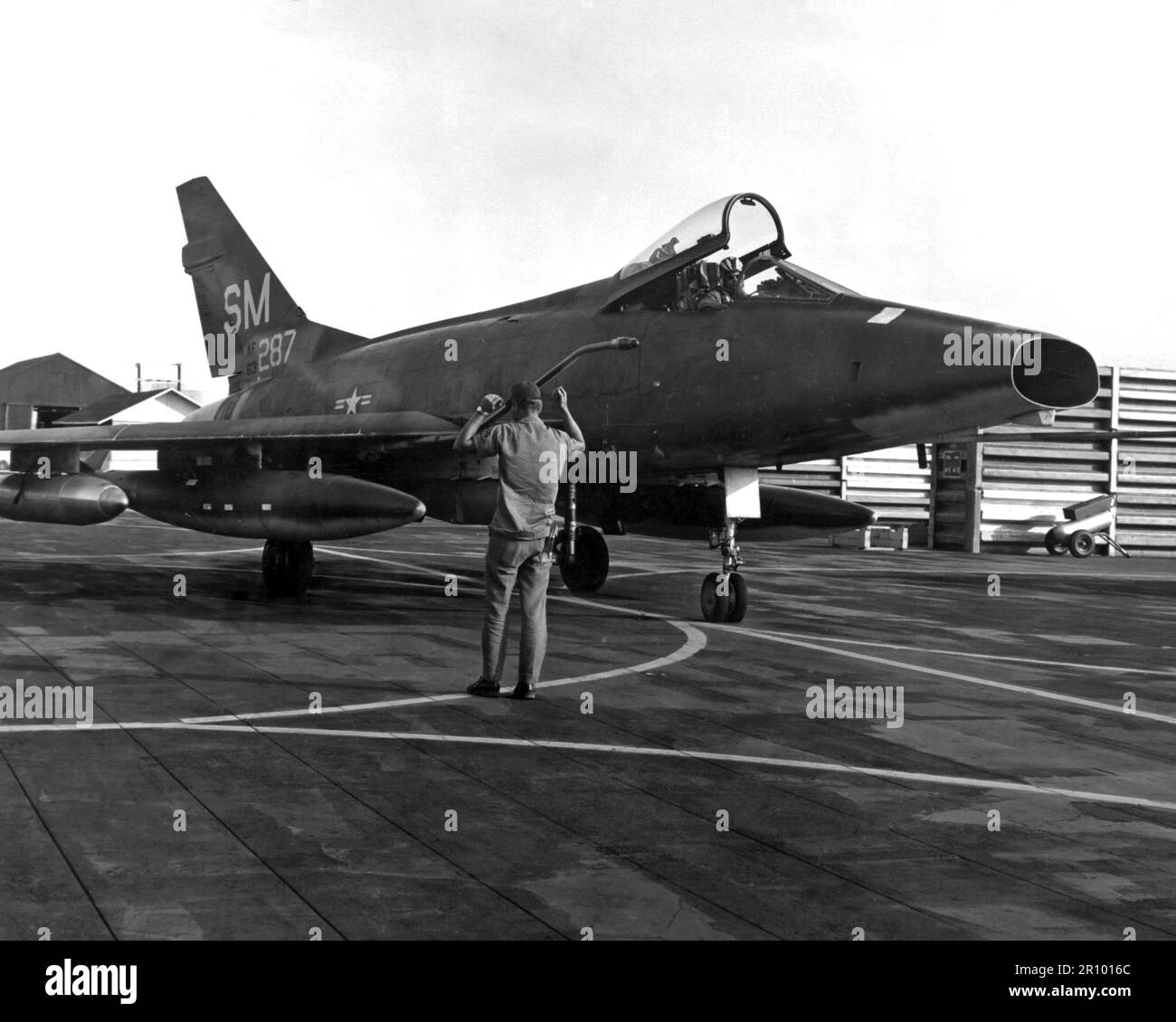 An Air Force Sergeant guides a 31st Tactical Fighter Wing F-100 Super Sabre aircraft into its fortified parking place, following a close air support mission over South Vietnam.  Wing pilots flew 23,069 sorties since deploying to Vietnam one year ago. Stock Photo