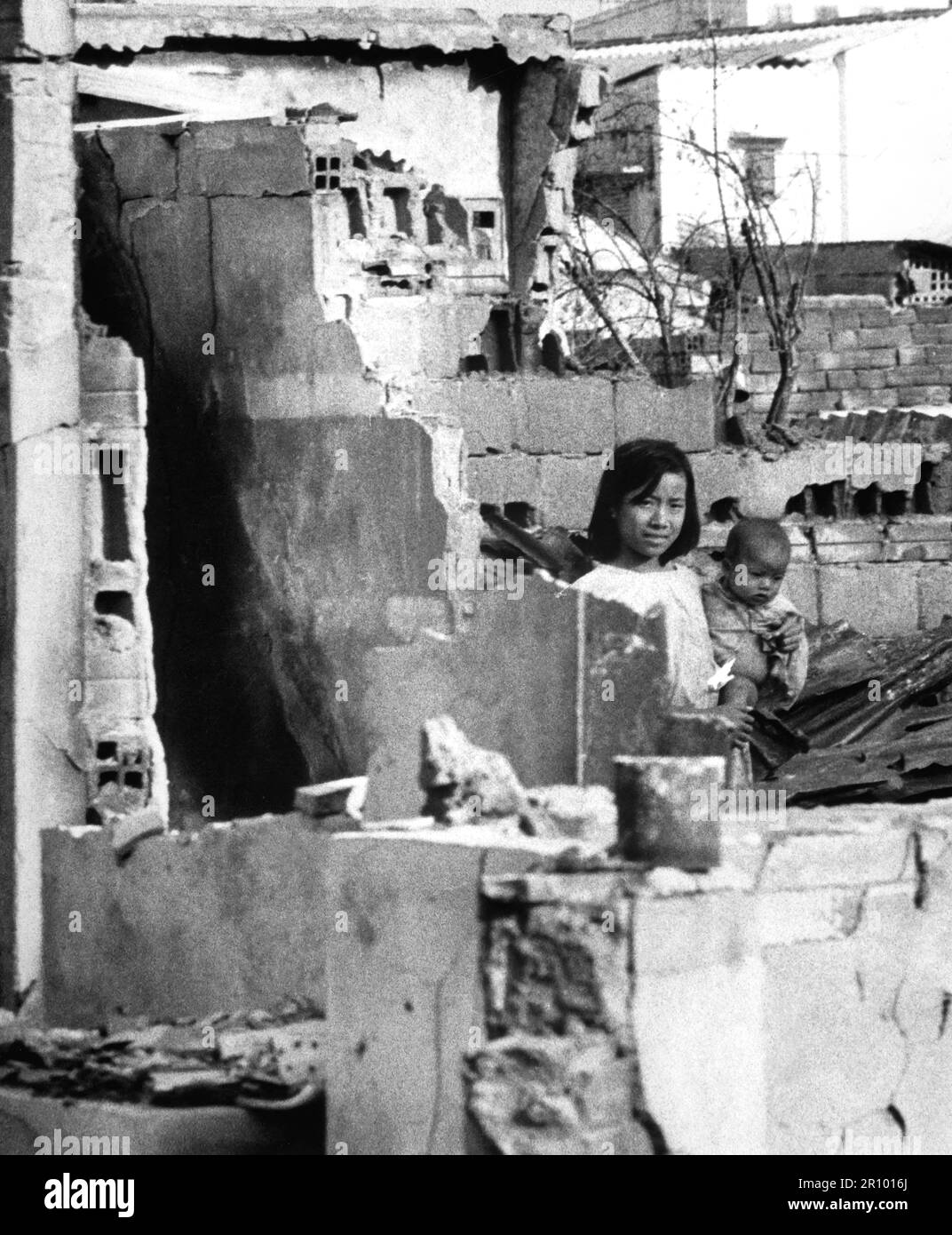 A girl, holding a small child, stands in the ruins of their Saigon home after a Viet Cong attack on January 31, 1968. Stock Photo