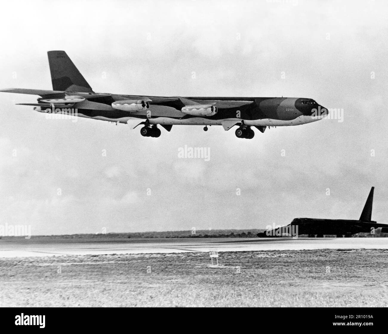 A B-52D Stratofortress aircraft waits beside the runway as a B-52G approaches for landing after completing a bombing mission over North Vietnam during Operation LINEBACKER.  The aircraft are from the Strategic Air Command. Stock Photo