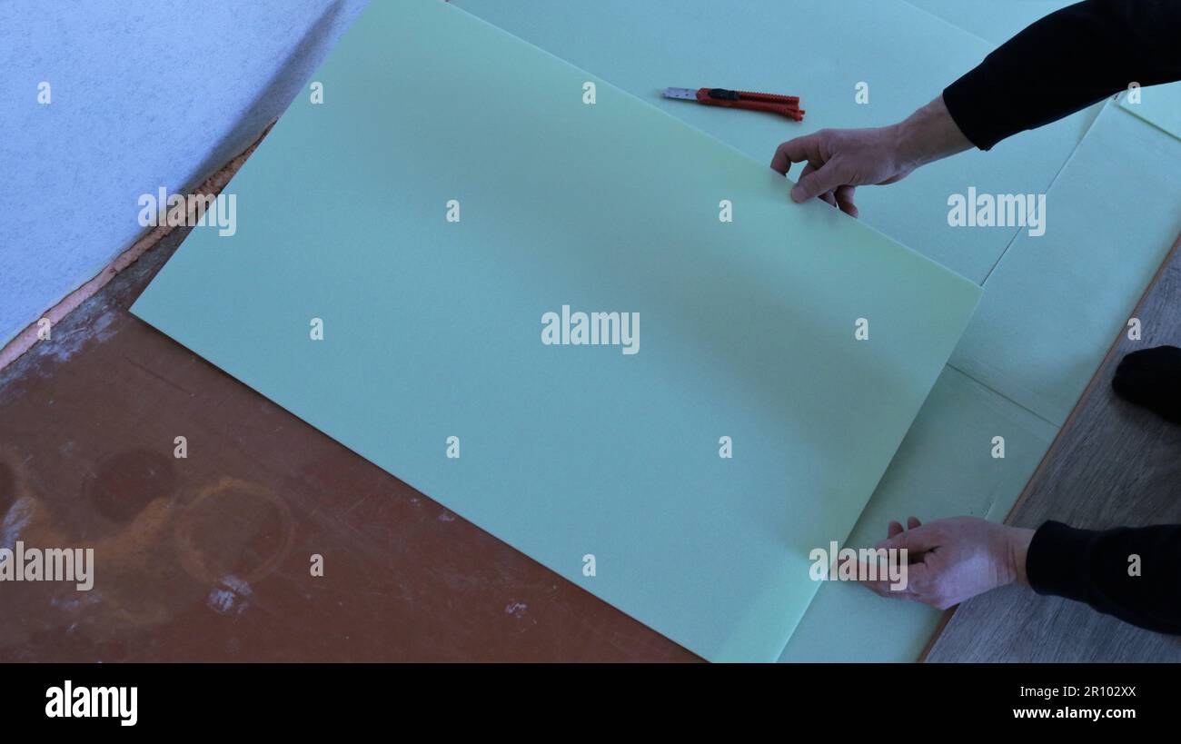 a man lays out a soft material used for laying under a laminate in the process of covering the floor in a room, using a special substrate for laminate Stock Photo