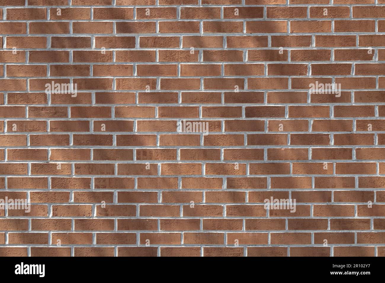Close up texture background of a modern traditional exterior red clay brick wall in running bond (stretcher bond) pattern, with diagonal shadows Stock Photo