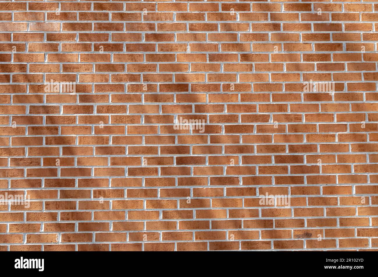 Close up texture background of a modern traditional exterior red clay brick wall in running bond (stretcher bond) pattern, with diagonal shadows Stock Photo