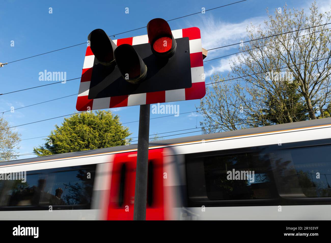 Warning lights at Church Lane crossing. Railway level crossing with Greater Anglia train passing through at speed. Red light, stop light Stock Photo