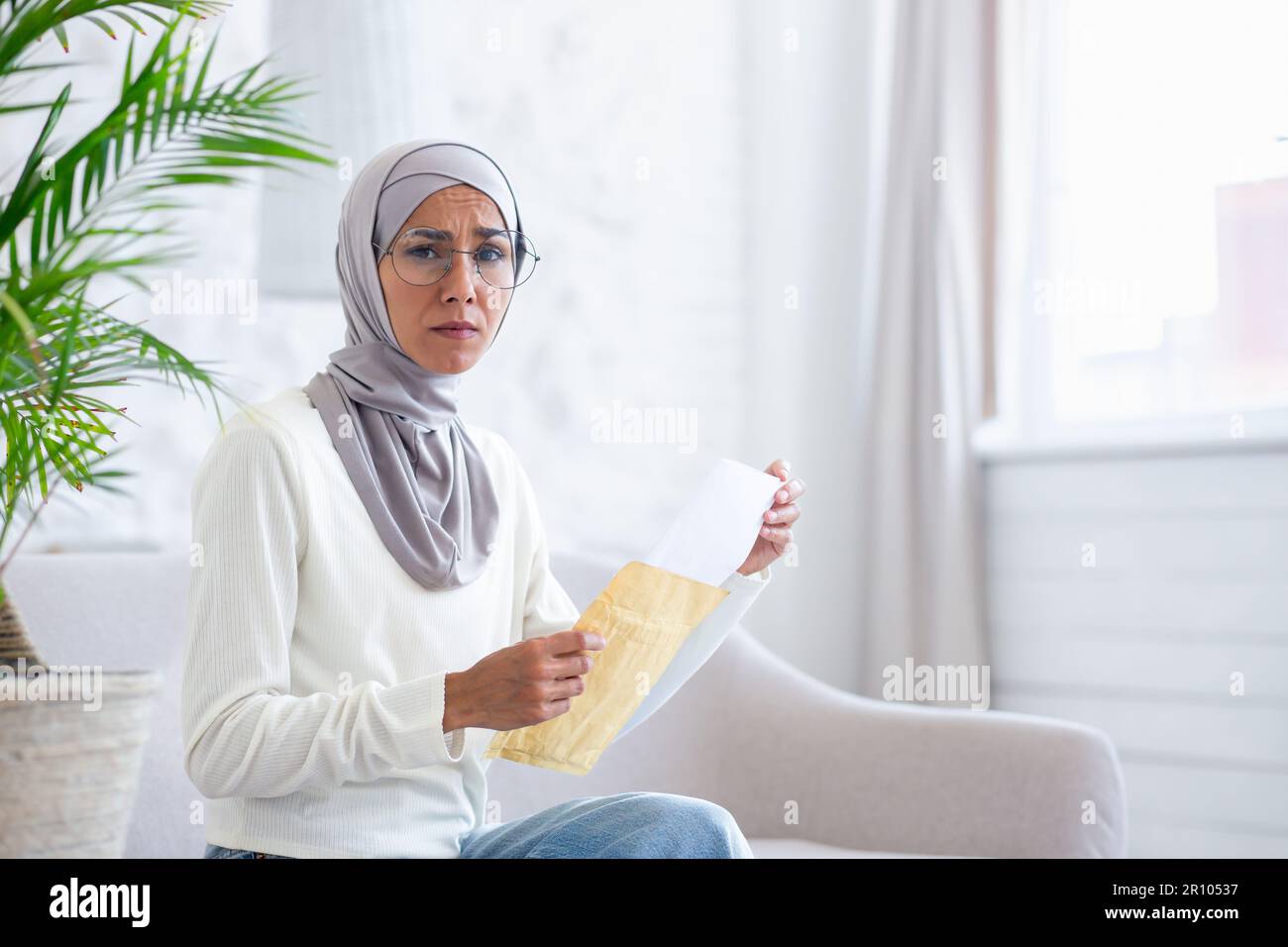 Upset and worried young woman in hijab sitting on sofa at home and ...