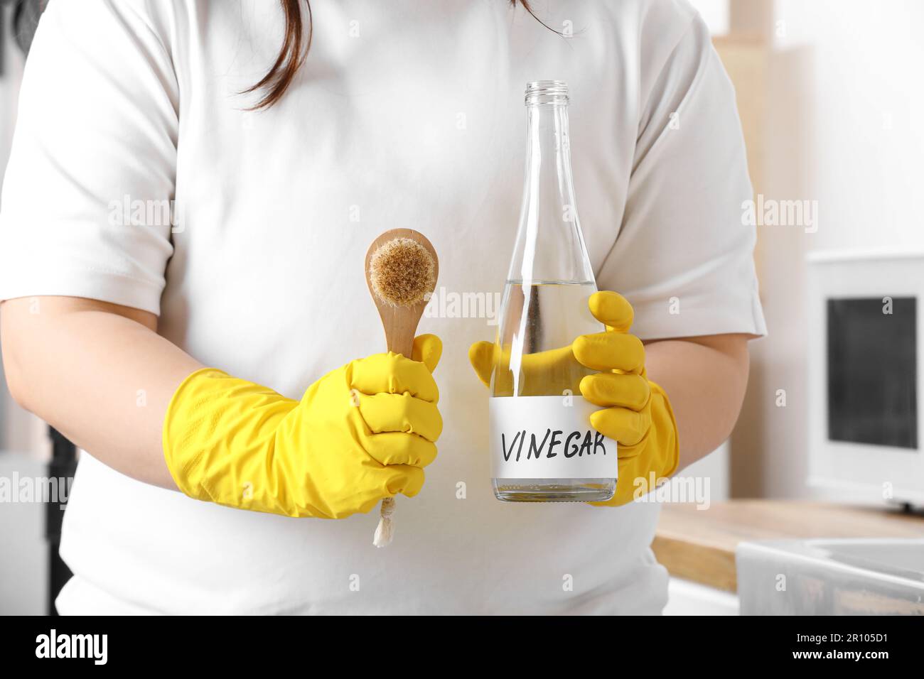 Woman in rubber gloves with bottle of vinegar and brush in kitchen
