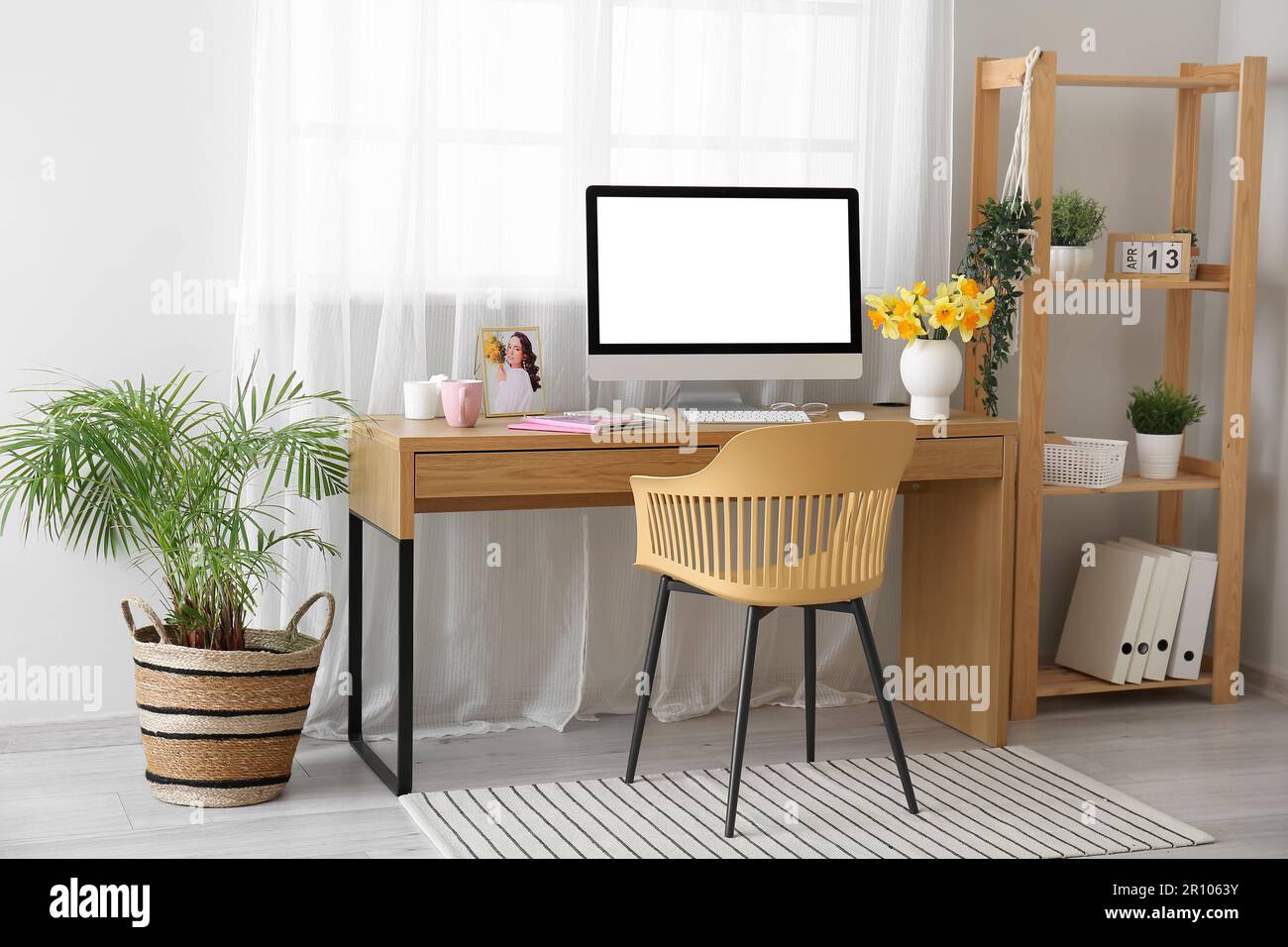 Comfortable workplace with modern PC, shelving unit and narcissus ...
