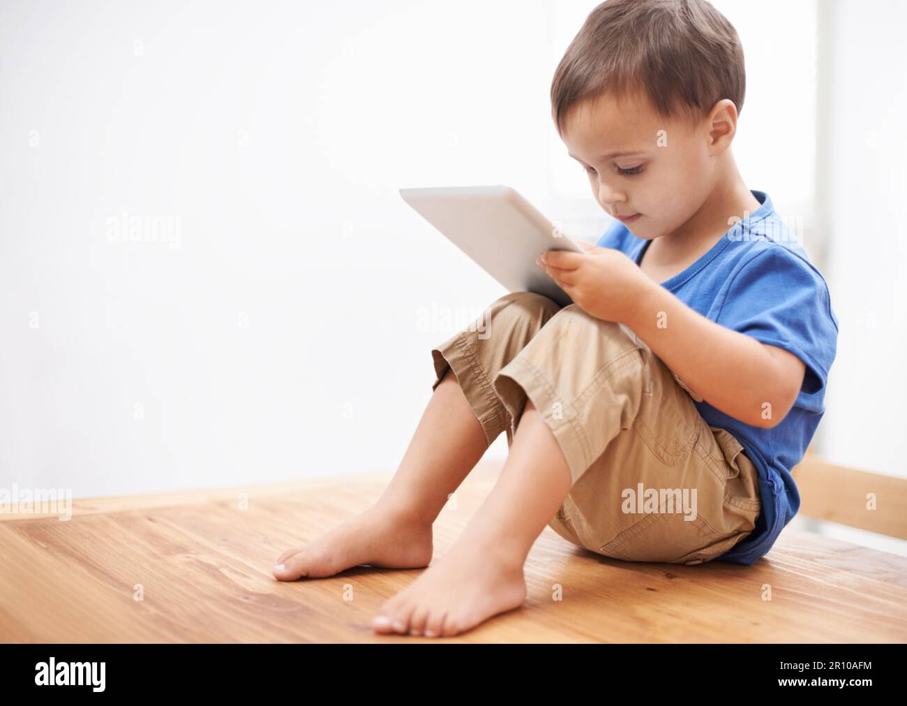 I wonder how this works. a young boy sitting on a table playing with a digital tablet. Stock Photo